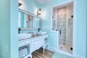 A bathroom with a white vanity, a large mirror, and a shower with a wavy tile design.