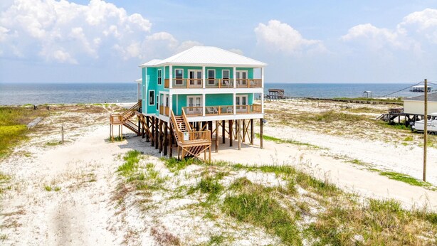 A two-story beach house with a balcony, wooden deck, and a view of the ocean.