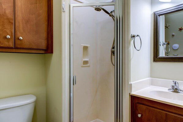 Un baño con ducha, inodoro, tocador y espejo.