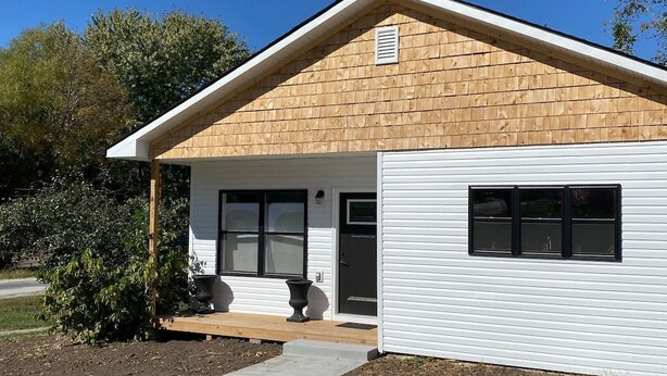 A single-story building with a gabled roof, a front porch, and a garage door.