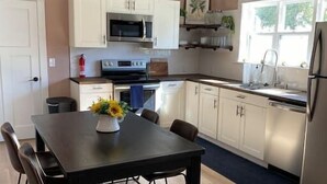 A modern kitchen with white cabinets, stainless steel appliances, and a dining area with a dark table and chairs.