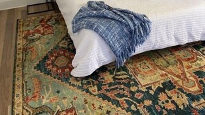 A bedroom with a bed, a patterned rug, two bedside tables, and a small plant.