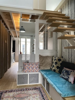 Una sala de estar moderna con un banco empotrado, un tapete estampado y una escalera con vigas de madera.