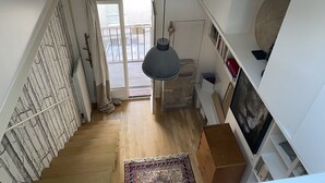 A staircase leading to a balcony with a hanging light fixture, wooden flooring, and a patterned rug.