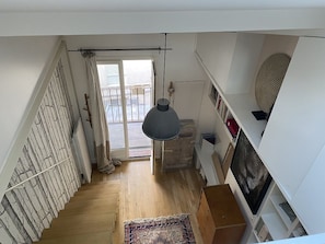 Una escalera conduce a un balcón con una lámpara colgante, piso de madera y un tapete estampado.