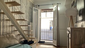 A bedroom with a bed, a sofa, a wooden staircase, a wardrobe, and a view of the outside.