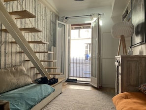 Un dormitorio con cama, sofá, escalera de madera, armario y vistas al exterior.