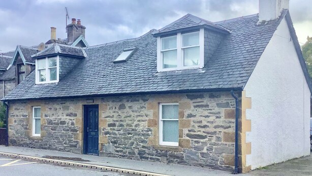 A stone house with a dark roof, a chimney, and a blue door. - Comfy 3-bedroom Cottage in Newtonmore, Cairngorms (Newtonmore)