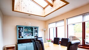 A dining area with a wooden table and chairs, a blue cabinet with glass doors, and a view of the outdoors through large windows. - Comfy 3-bedroom Cottage in Newtonmore, Cairngorms (Newtonmore)