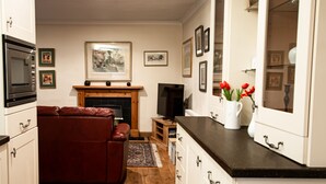 A modern kitchen with white cabinets, a black countertop, and a fireplace. There is a red leather sofa and a television in the living area. - Comfy 3-bedroom Cottage in Newtonmore, Cairngorms (Newtonmore)