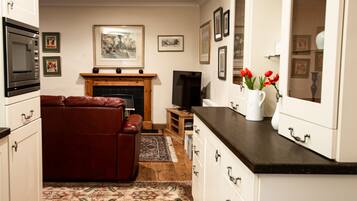 A modern kitchen with white cabinets, a black countertop, and a fireplace. There is a red leather sofa and a television in the living area.