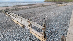 A pebbled beach with a wooden fence and a grassy hill in the background. - 3 bedroom accommodation in St Bees, near Whitehaven (St Bees, near Whitehaven)