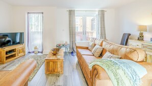 A living room with a wooden coffee table, a sofa, a TV on a wooden stand, and a view through a glass door to an outdoor area. - 3 bedroom accommodation in St Bees, near Whitehaven (St Bees, near Whitehaven)