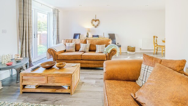A living room with a sofa, coffee table, and a dining area with chairs. - 3 bedroom accommodation in St Bees, near Whitehaven (St Bees, near Whitehaven)