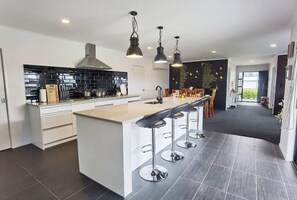 A modern kitchen with a central island, bar stools, and pendant lighting. - House of Hope - Spa Pool, Sleeps 12 (Rotorua)