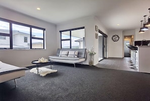 A modern living room with a grey sofa, a small round table, and a white fluffy rug. - House of Hope - Spa Pool, Sleeps 12 (Rotorua)