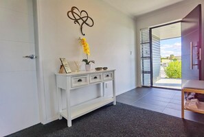 A hallway with a white console table, a decorative wall piece, and a view through a glass door.