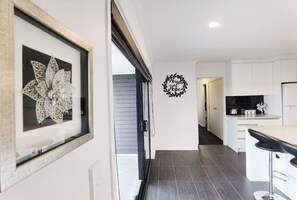A modern kitchen with white cabinets, a black countertop, and a framed artwork on the wall. - House of Hope - Spa Pool, Sleeps 12 (Rotorua)