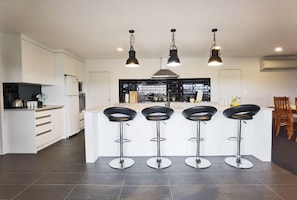 A modern kitchen with white cabinets, a central island with bar stools, and pendant lighting. - House of Hope - Spa Pool, Sleeps 12 (Rotorua)
