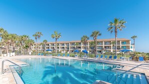 Un hotel con piscina, palmeras y sombrillas azules.