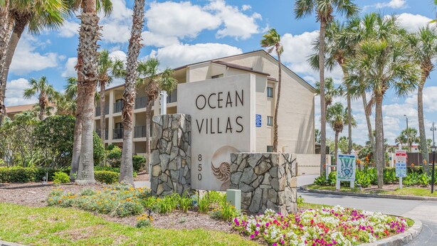Letrero de Ocean Villas con base de piedra y cielo despejado al fondo.