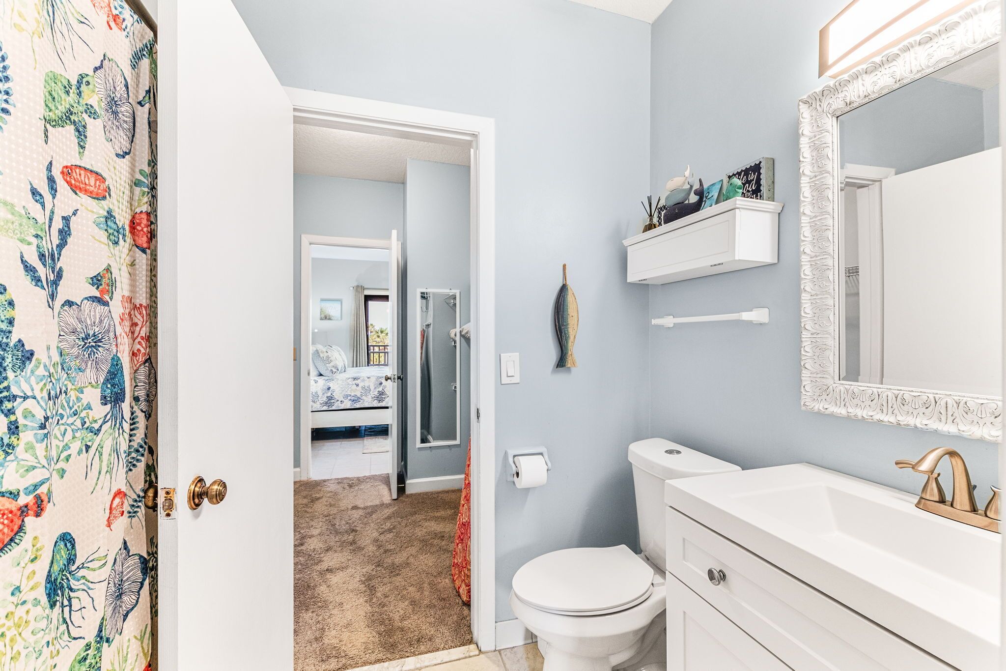 A bathroom with a toilet, sink, and mirror. There is a shower visible in the background.