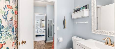 A bathroom with a toilet, sink, and mirror. There is a shower visible in the background.