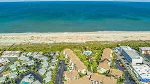 Vista aérea de una zona residencial costera con playa, estacionamiento y un edificio con piscina.