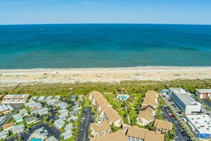 Vue aérienne d’un quartier résidentiel situé sur la côte, avec une plage, un parking et un immeuble doté d’une piscine.