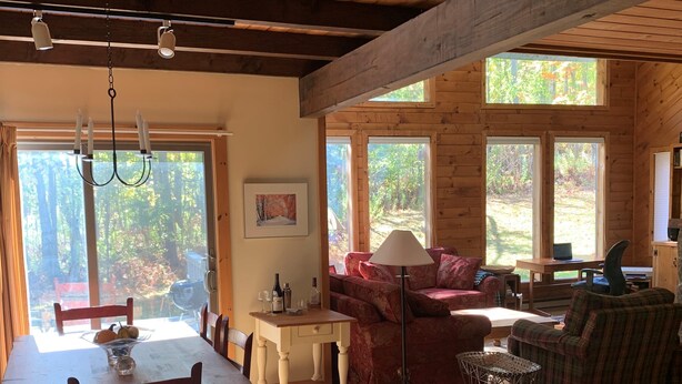 A cozy cabin interior with a dining table, red sofa, and plaid armchair.