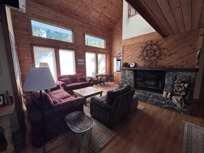 A cozy cabin interior with a fireplace, wooden walls, and a seating area with a couch and chairs.