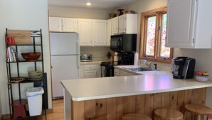 A kitchen with white cabinets, a black microwave, a stainless steel sink, and wooden stools.