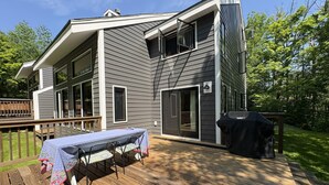 A two-story house with a deck, a barbecue grill, and a covered table.