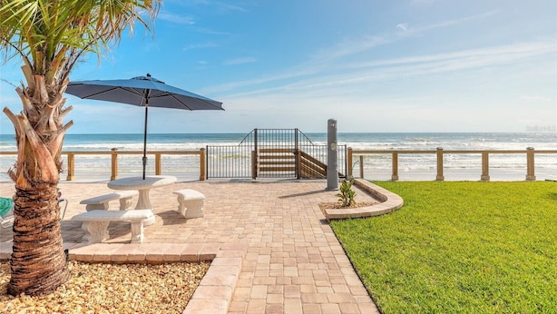 A patio with a table and chairs, a palm tree, and a view of the ocean. - Oceanfront Paradise Awaits You! Walk directly to the beach from property (New Smyrna Beach)
