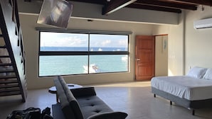 Une chambre avec une grande fenêtre donnant sur la mer, un lit, un canapé et un téléviseur fixé au plafond.
