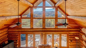 Una cabaña de troncos con techo alto, ventanas grandes y vistas a las montañas.
