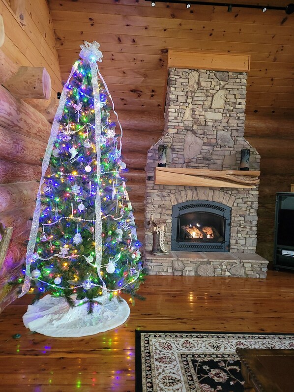 Un árbol de Navidad con luces de colores y adornos, una chimenea de piedra y paredes de madera.