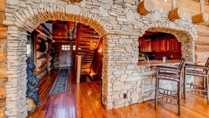 Interior de una cabaña de troncos con paredes de piedra, piso de madera y chimenea de piedra.