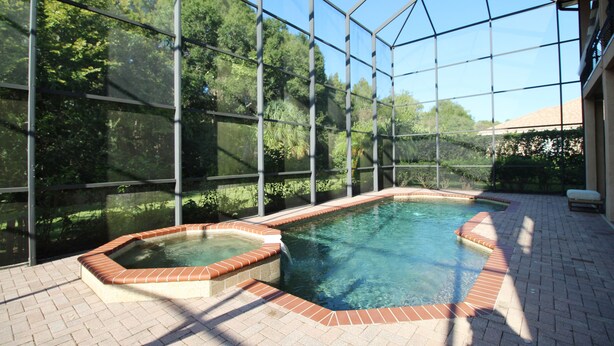 Une piscine entourée d’une véranda en verre et bordée d’une terrasse en briques.