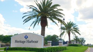 Une enseigne indiquant l’entrée de Heritage Harbour, avec un ciel dégagé et des palmiers en arrière-plan.