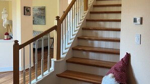 Un escalier en bois avec des rampes blanches et une décoration représentant un Père Noël en peluche au bas de l’escalier.