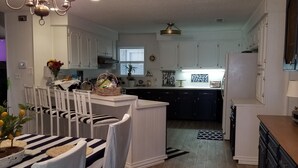 Une cuisine moderne avec des meubles blancs, un coin repas avec des nappes à rayures et des chaises blanches, et un lustre.