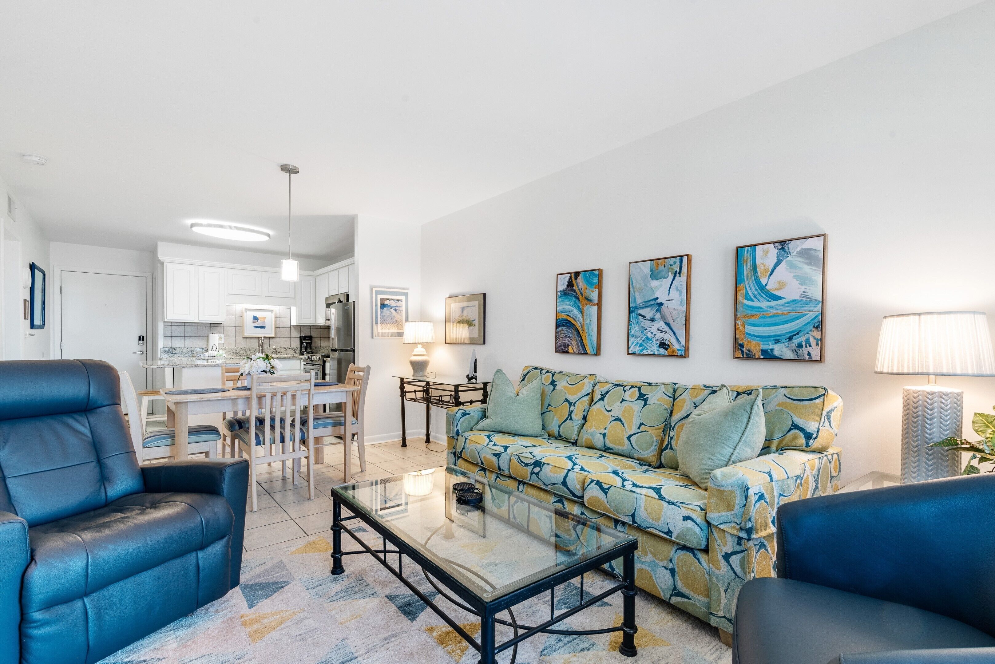 A modern living room with a sofa, two armchairs, a glass coffee table, and a dining area with a table and chairs.