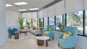 A spacious lounge area with large windows, comfortable seating, and potted plants. - Gulf Shores Plantation-East 3210 (Gulf Shores)