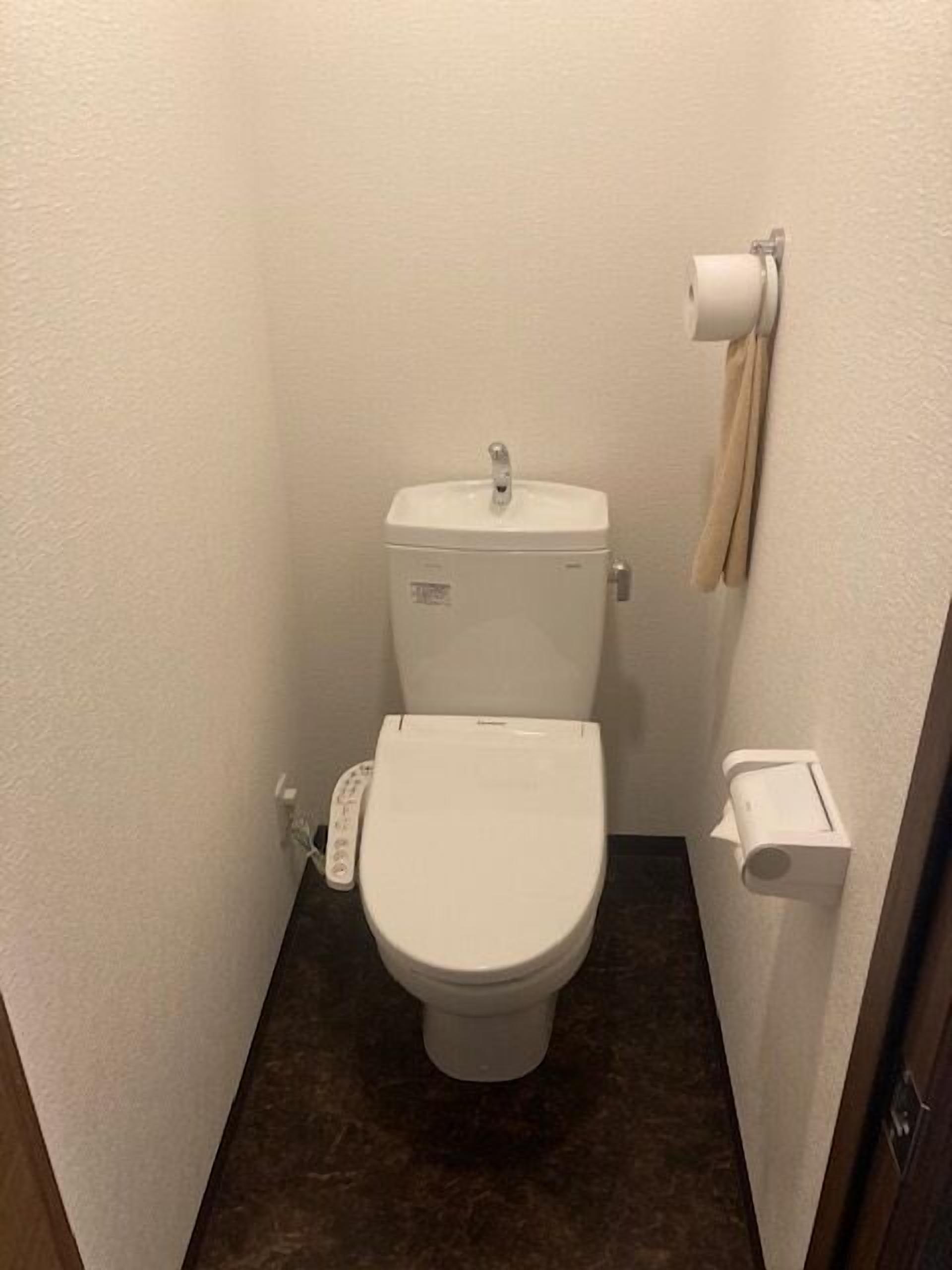 A small, compact bathroom with a white toilet, a paper towel dispenser, and a toilet paper holder on the wall.