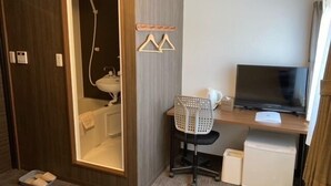 Une chambre d’hôtel équipée d’un bureau en bois, d’une télévision, d’une chaise, d’un petit réfrigérateur, d’un lavabo et d’un espace douche.