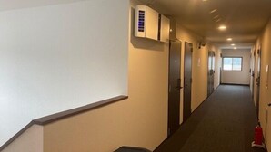 Un couloir d’hôtel avec un sol recouvert de moquette, une poubelle et un extincteur.