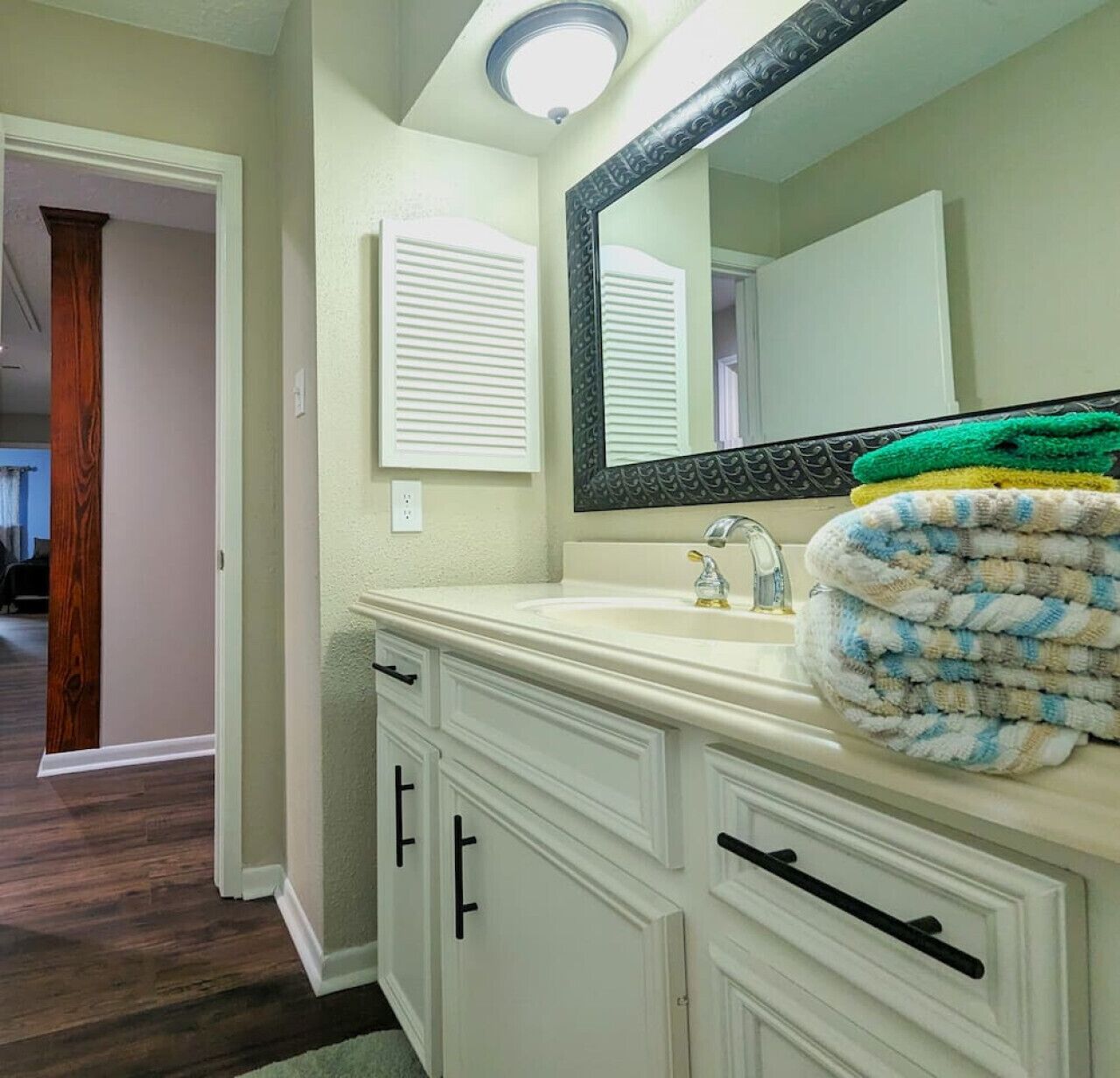 A bathroom with a white vanity, a large mirror, and a towel stacked on the counter.