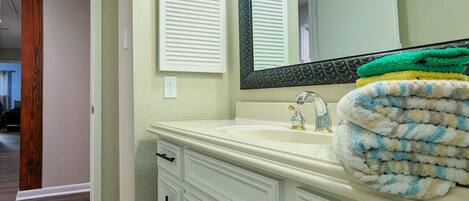 A bathroom with a white vanity, a large mirror, and a towel stacked on the counter.