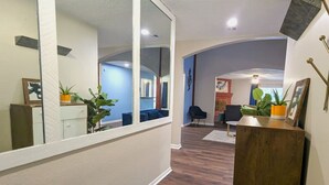 Passadís amb terra de fusta, un mirall, una taula de recepció de fusta i una habitació blava al fons.